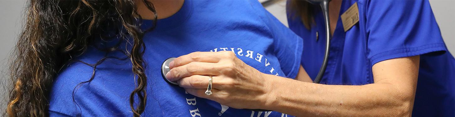 Nurse checking students heart beat with stethoscope